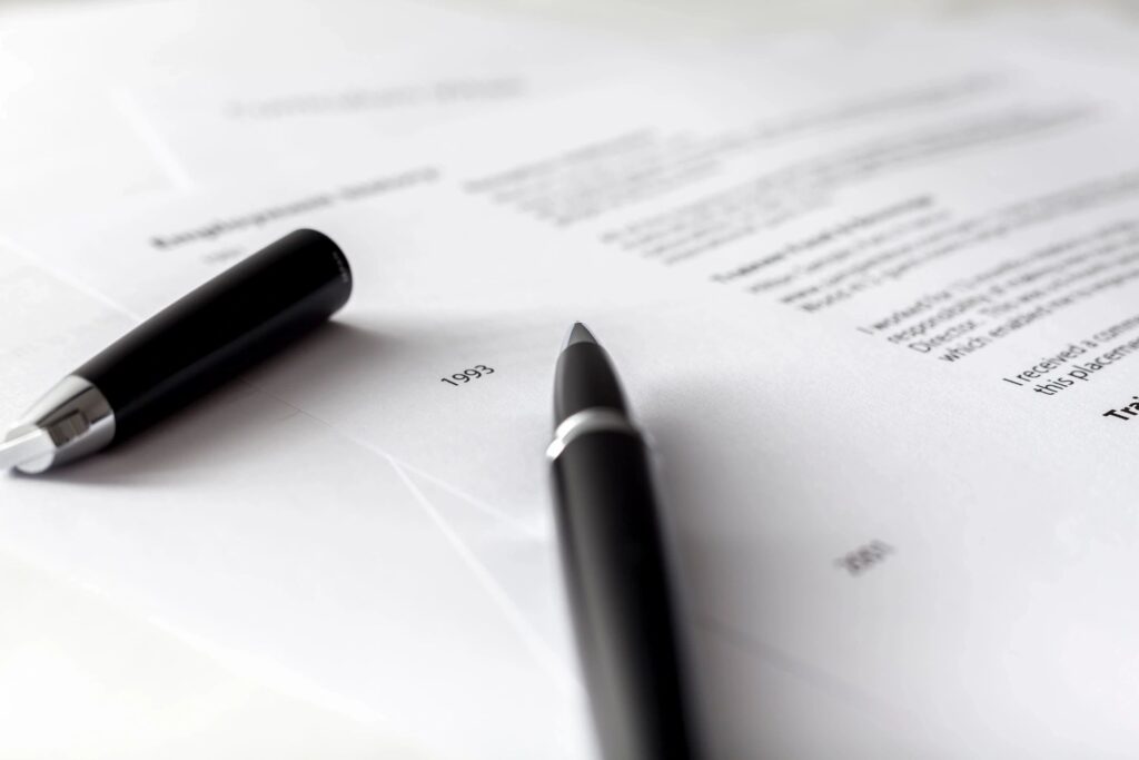 close up of blurred resume on white paper with a black pen on top of paper with it's black lid off and to the left of the pen.